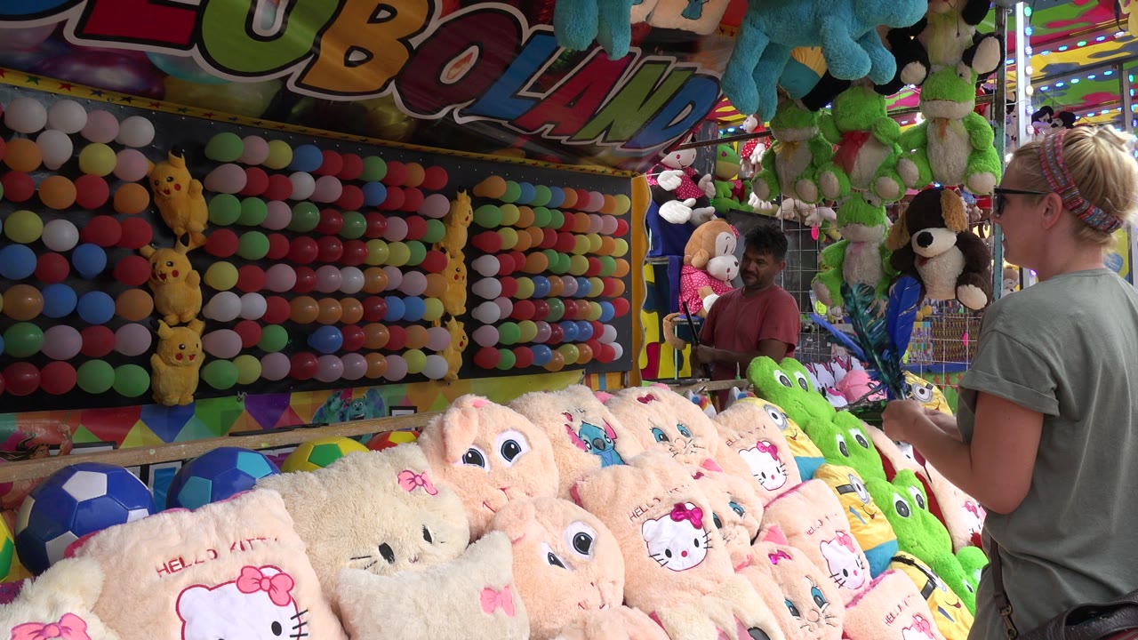 Woman aiming at a colorful balloon booth with plush prizes in front.