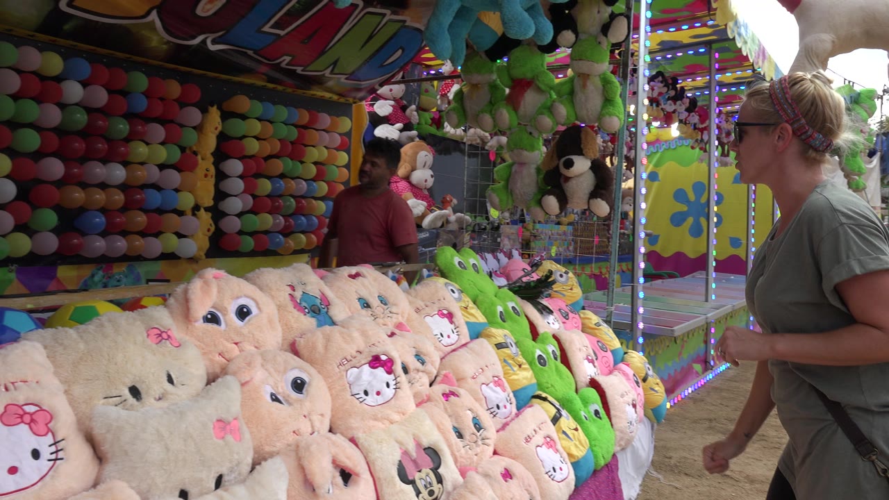 Woman at a carnival prize booth with plush toys and balloons.