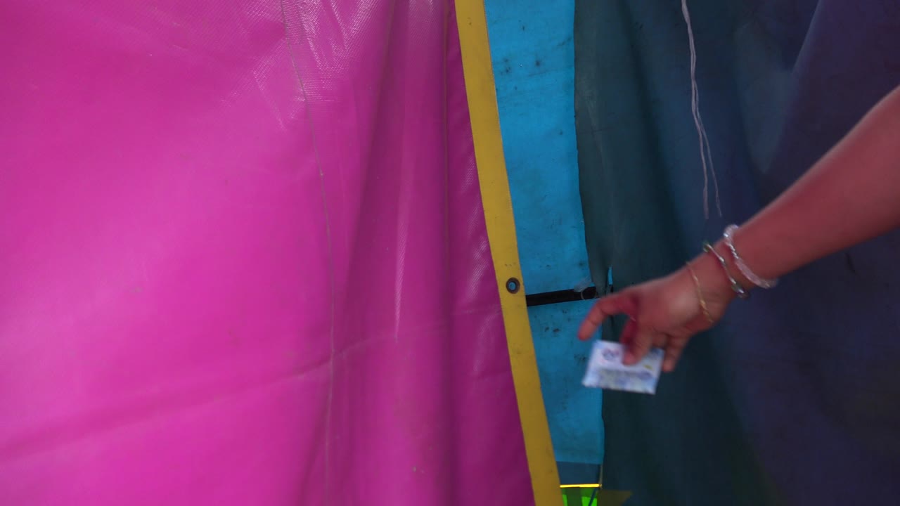 The second frame keeps the tight San Jose del Cabo composition on the pink tarp, yellow border, blue support, and a hand with bracelets holding a small paper closer to the dark fabric side.