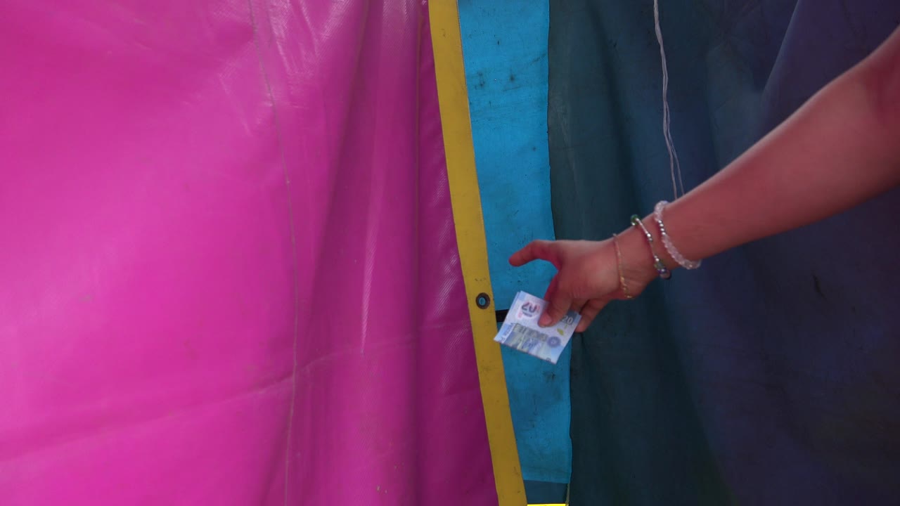 Bracelet-wearing hand points near a yellow-edged pink tarp
