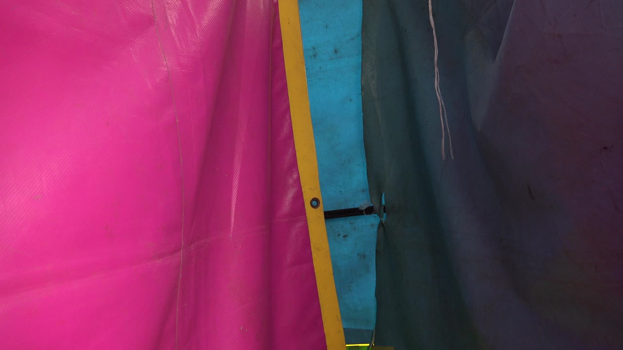 A similar close-up of the San Jose del Cabo tent wall shows the pink panel shifted wider in frame, with the yellow divider and blue fabric still visible, no visible people.