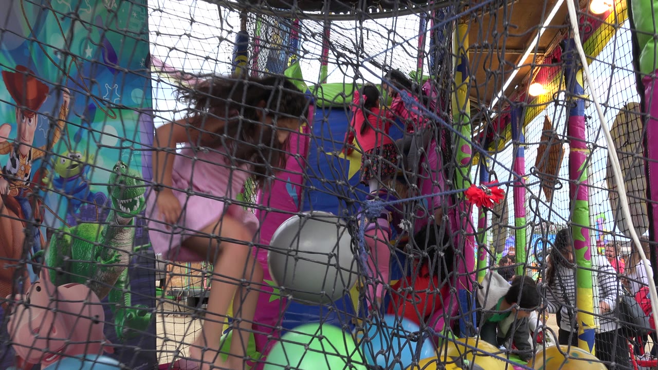 Girl in pink inside a netted inflatable play area with colorful balls.