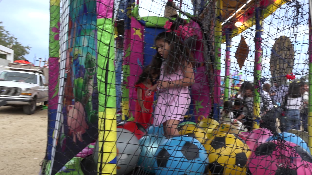 Children are visible through the black mesh as they play inside the colorful trampoline structure with large patterned balls in San Jose Del Cabo, Mexico.