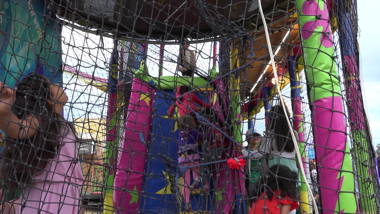 Children play behind black safety netting in a colorful bounce house in San Jose Del Cabo, Mexico, with bright inflatable posts filling the frame.