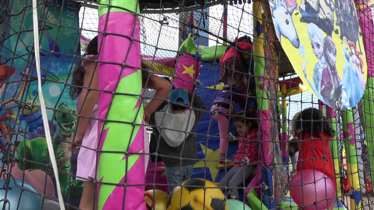 A child in a cap faces the play structure while other children climb and bounce near pink, green, blue, and yellow inflatable elements in San Jose del Cabo, Mexico.