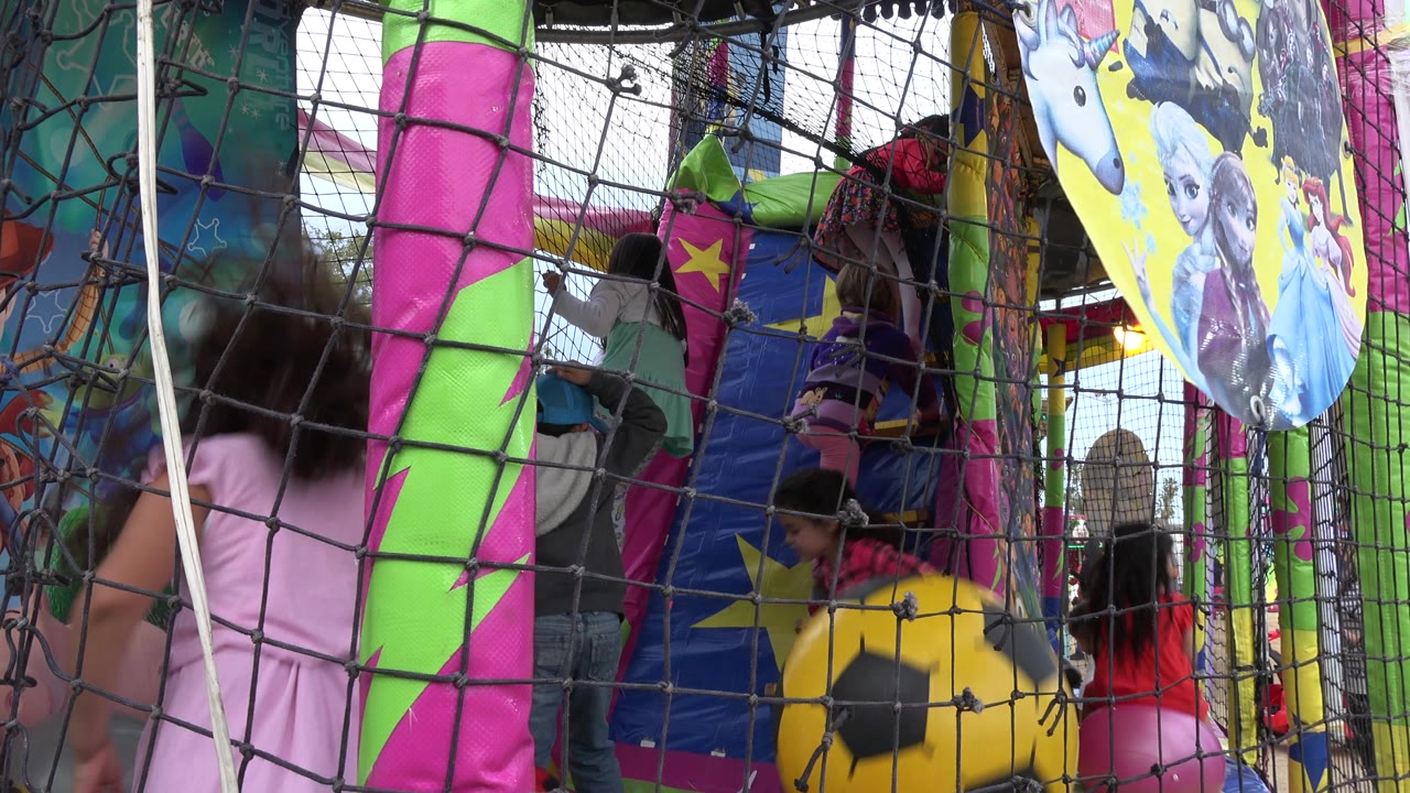 A child in pink passes close to the netted edge of the inflatable play area.