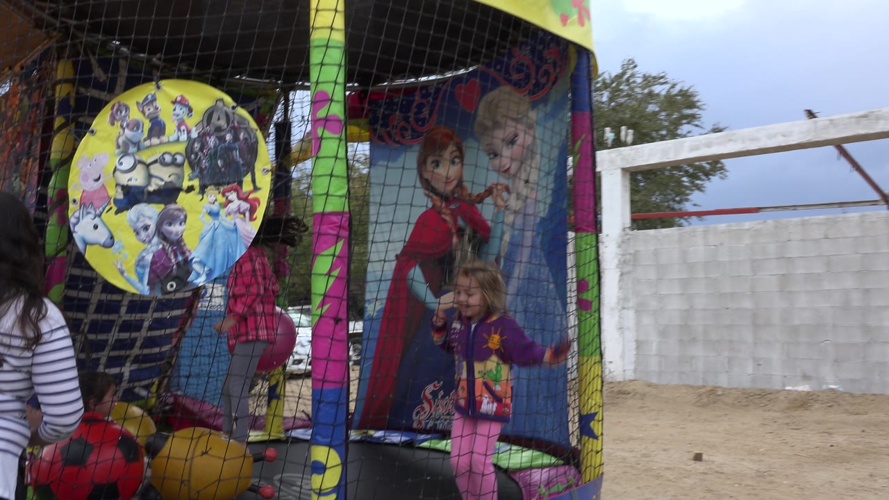 Children play inside a netted trampoline in San Jose del Cabo, Mexico, with a large yellow cartoon sign, bright plastic balls, and an adult partly visible at the left edge.