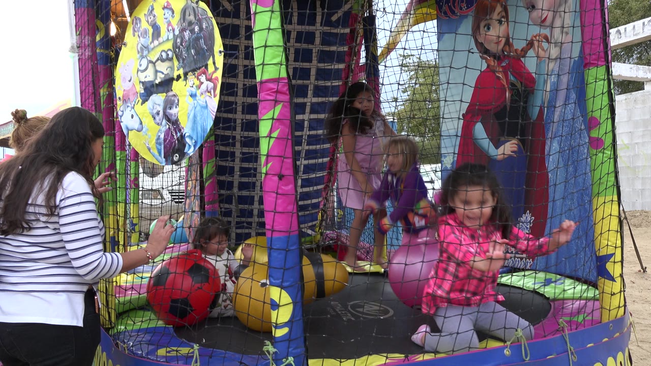 At 0:00 in San Jose del Cabo, Mexico, girls play behind the safety net of a colorful inflatable ball pit while an adult stands at the left edge watching them.