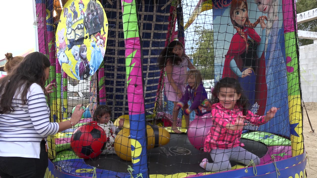 At 0:01 in San Jose del Cabo, Mexico, a girl in a pink plaid shirt smiles near the front net as other children stand and sit among balls inside the inflatable attraction.