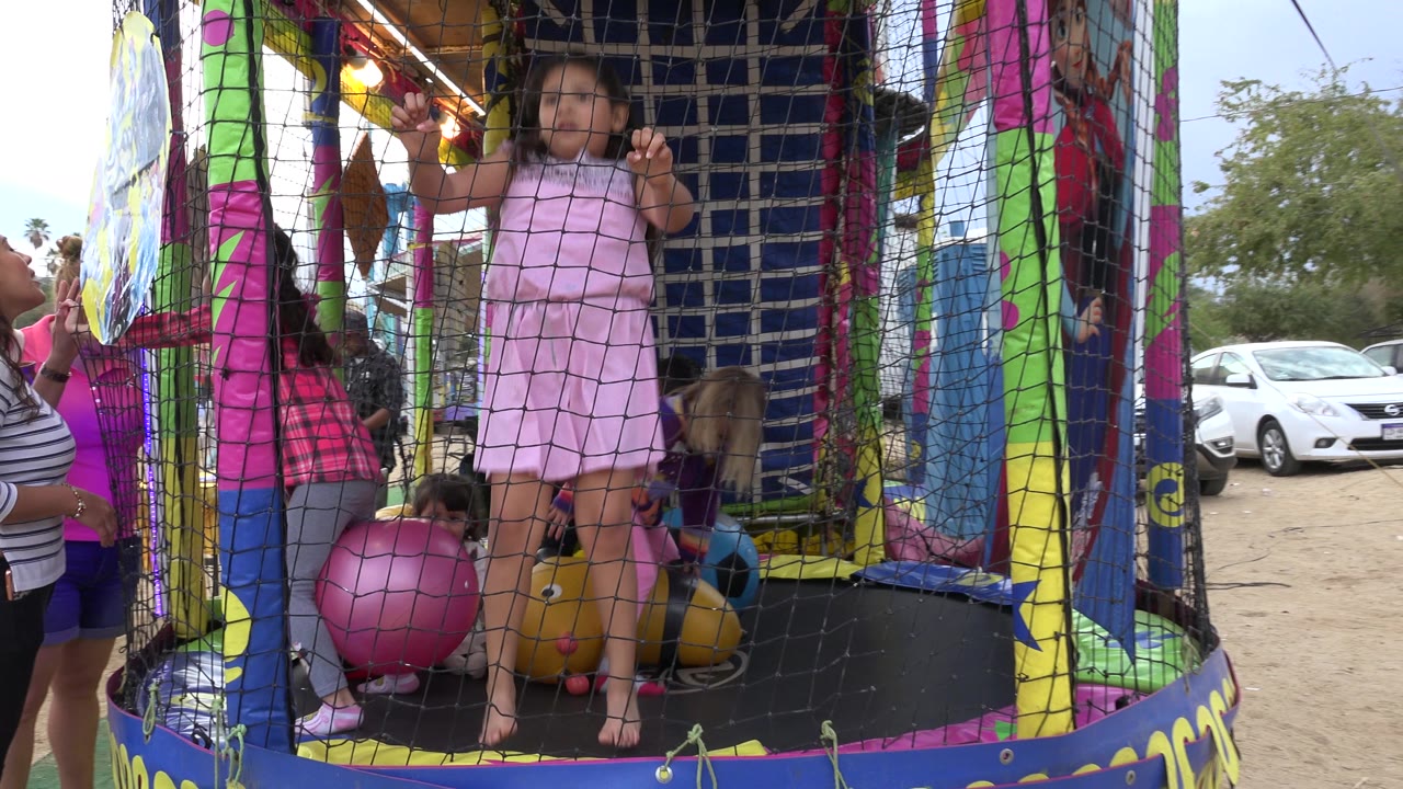 Child in pink dress standing inside a netted trampoline attraction