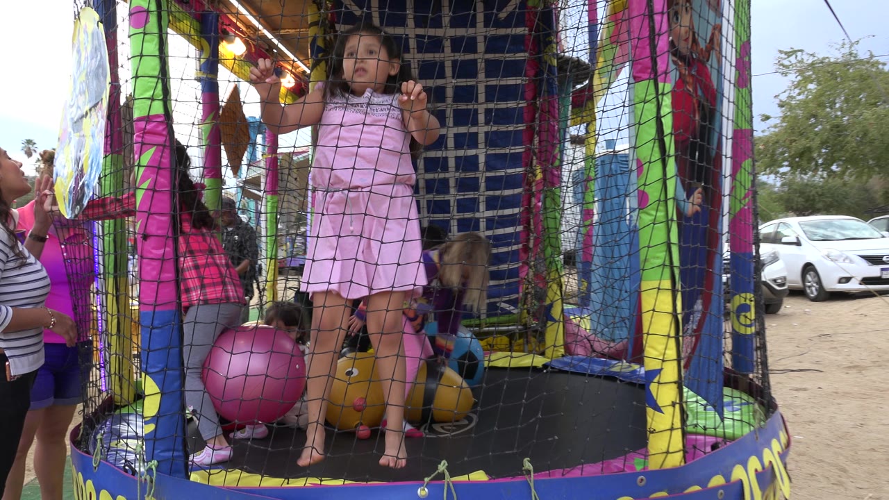 Children stand and crouch inside the netted trampoline area in San Jose Del Cabo, Mexico, while adults watch from just outside the enclosure.