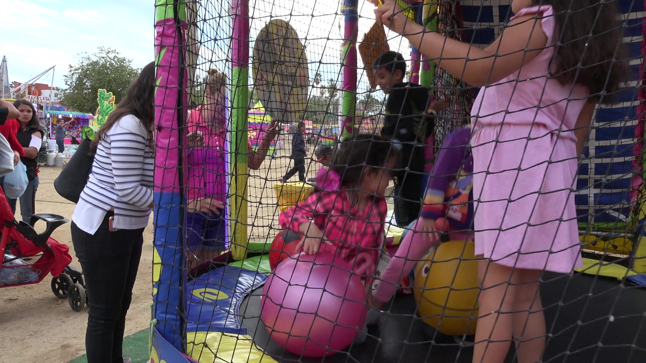 Children inside a netted inflatable play structure with adults nearby.
