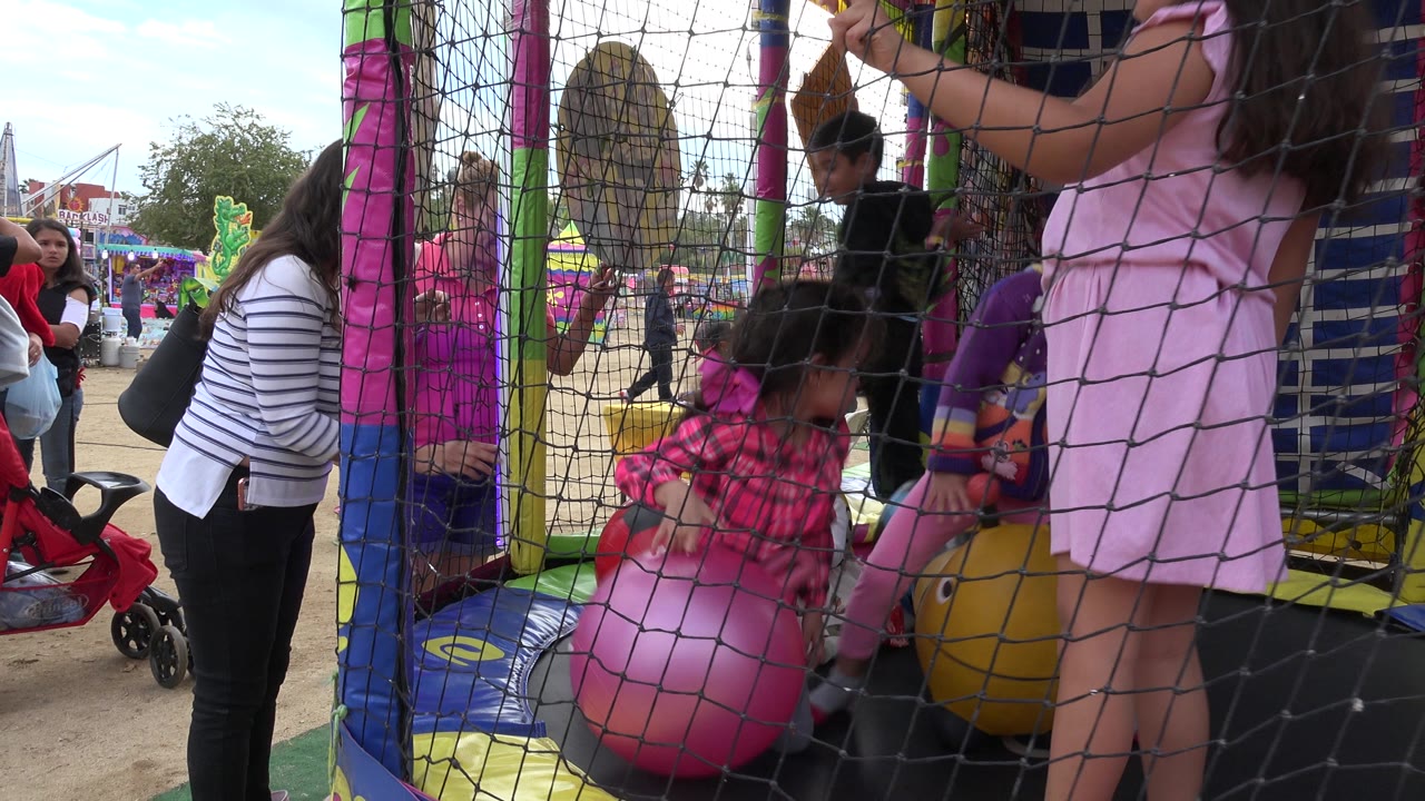 Children inside the San Jose Del Cabo inflatable play area move around oversized pink and yellow balls while black safety netting fills the foreground.