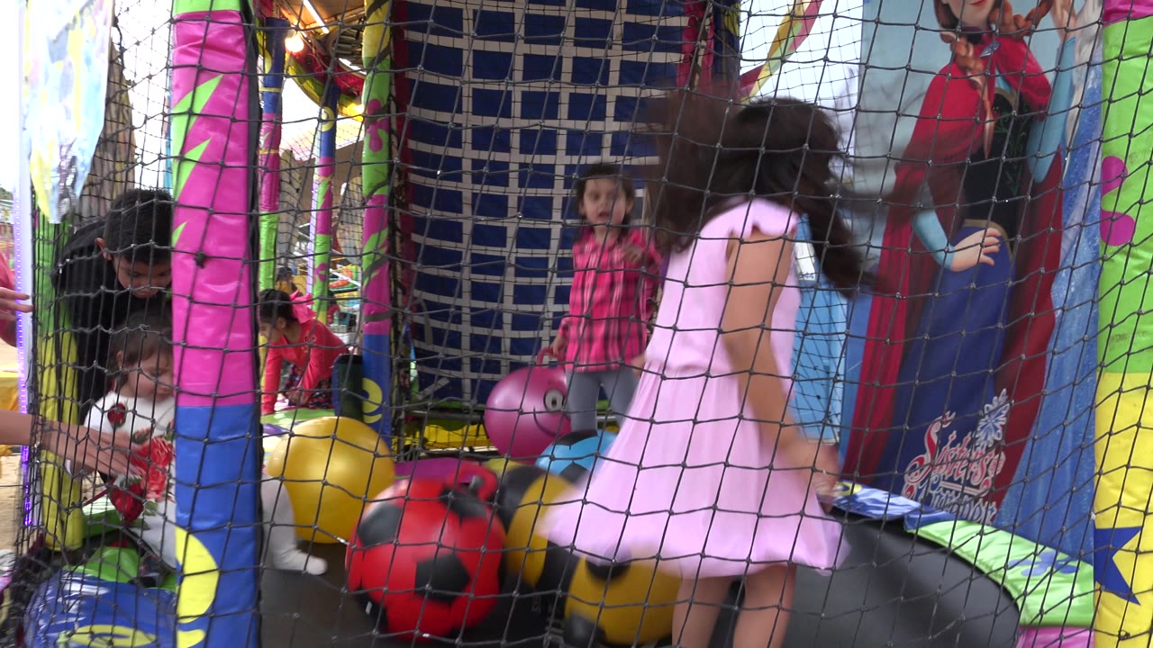 At 0:00 in San Jose del Cabo, Mexico, children stand and bounce inside a netted trampoline enclosure while adults lean in near red and yellow play balls.