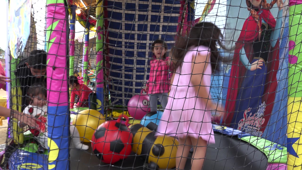 At 0:01 in San Jose del Cabo, Mexico, a girl in a pink dress moves in the foreground of the netted trampoline as another child stands near the back and adults stay close to the side.