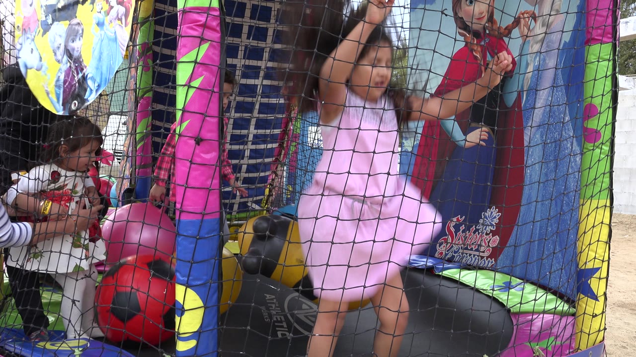 Children play behind a black safety net inside a colorful inflatable attraction in San Jose del Cabo, Mexico, with a child in a pink dress near the center and soccer-ball shapes below.
