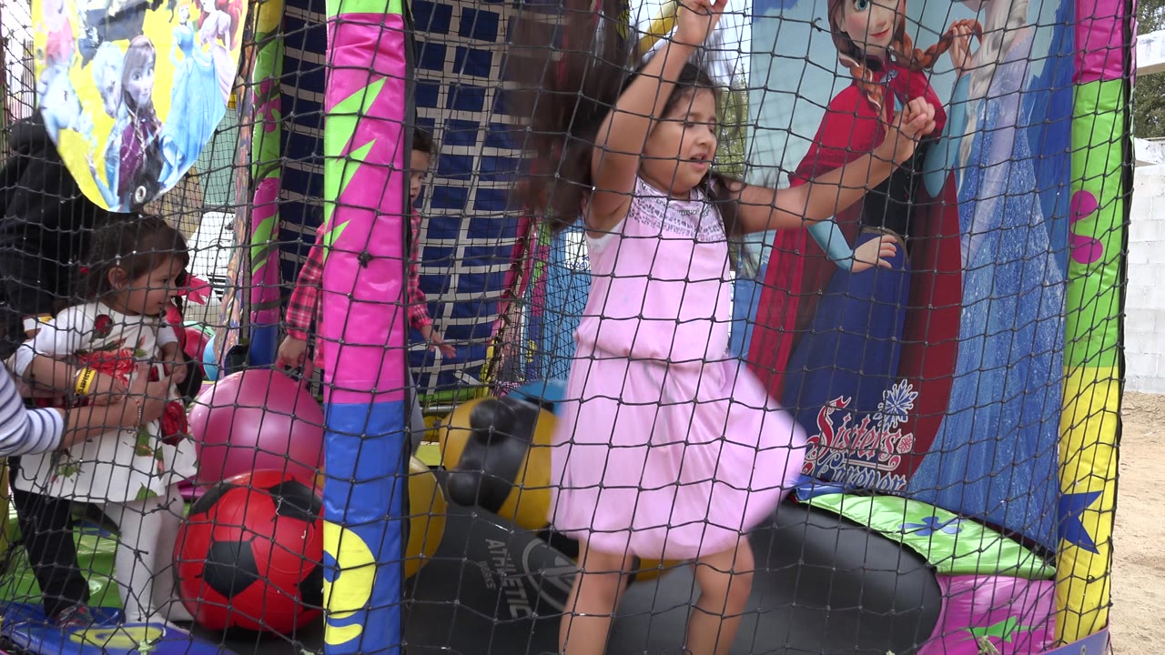 A girl in a pink dress stands close to the safety net in San Jose del Cabo, Mexico, with another small child and red and yellow soccer-ball shapes visible beside her.