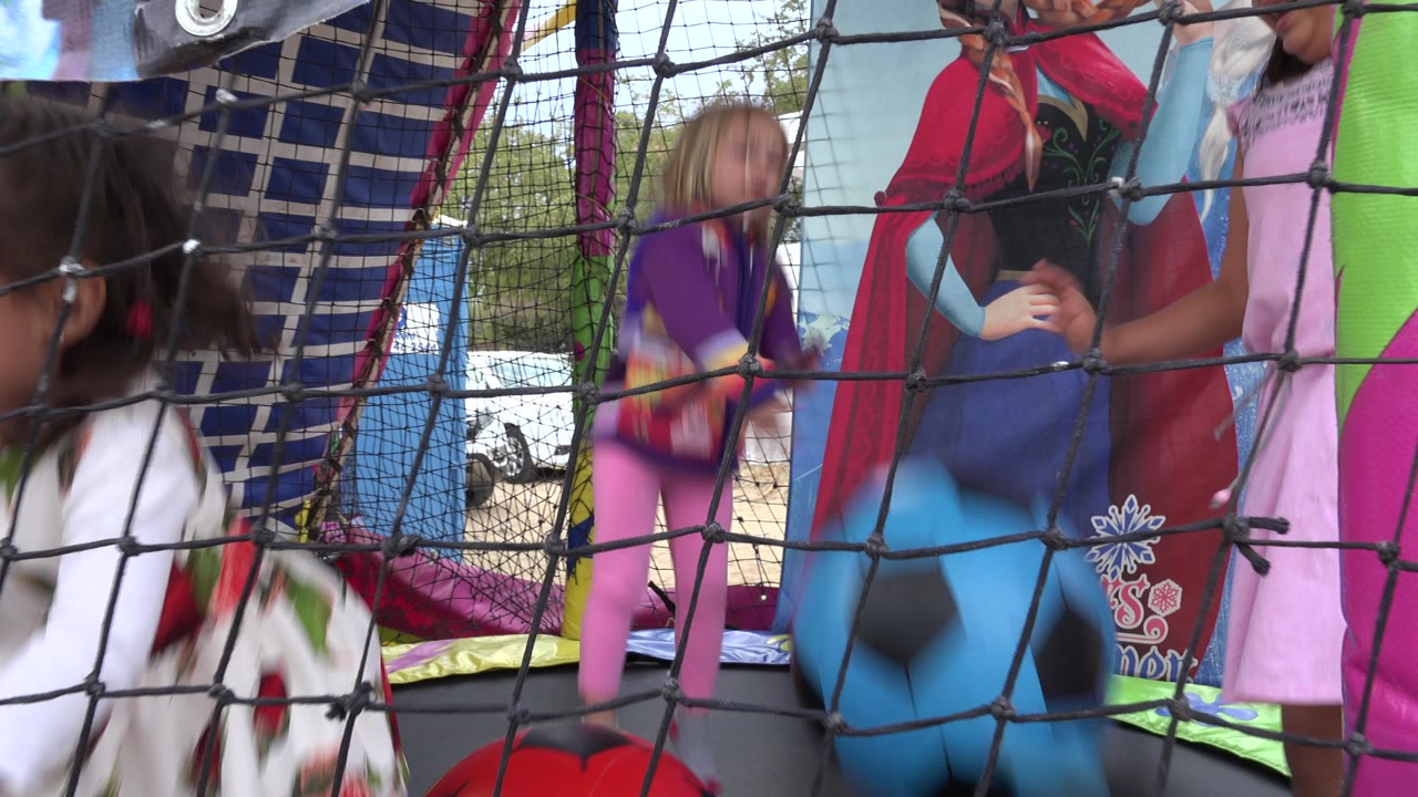 Children bouncing behind a rope net inside a colorful inflatable play area.