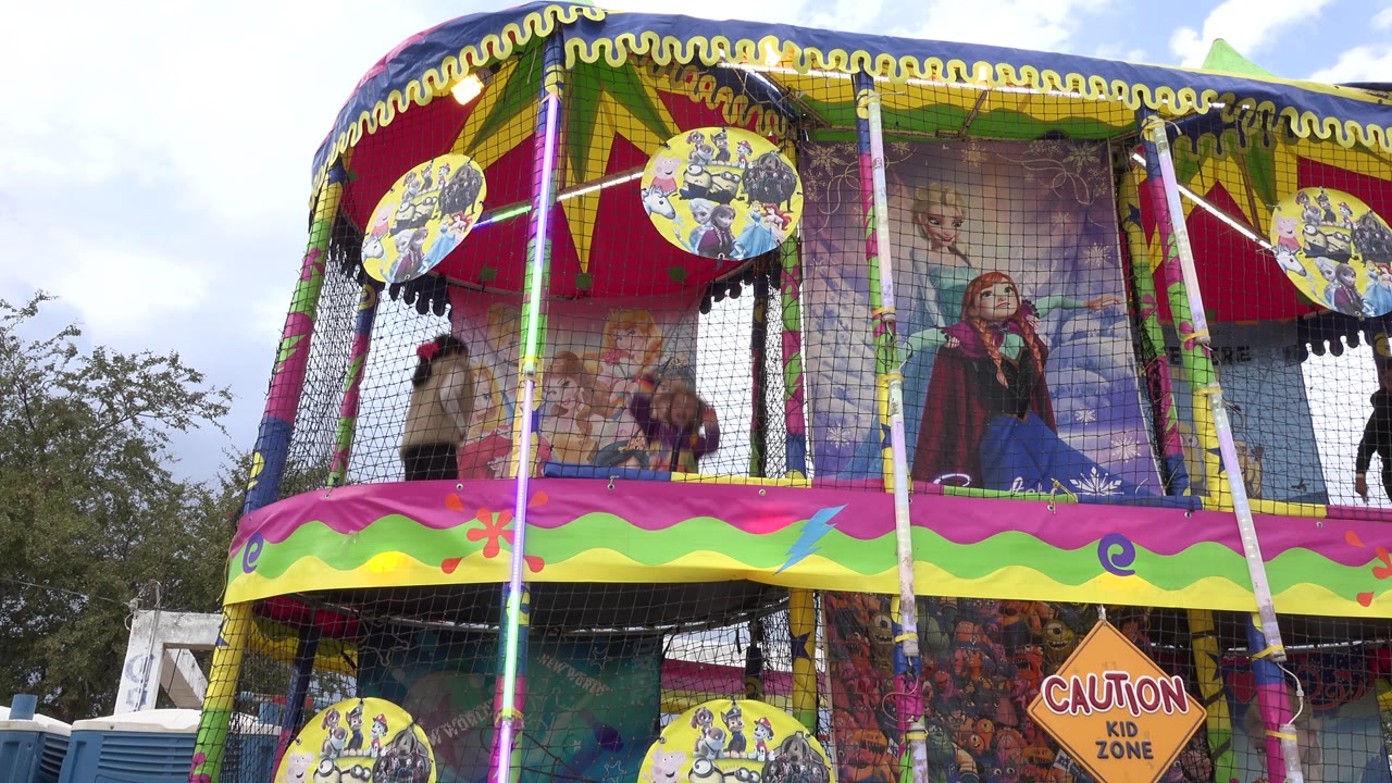 Wide view of a colorful bounce attraction with children behind safety netting.