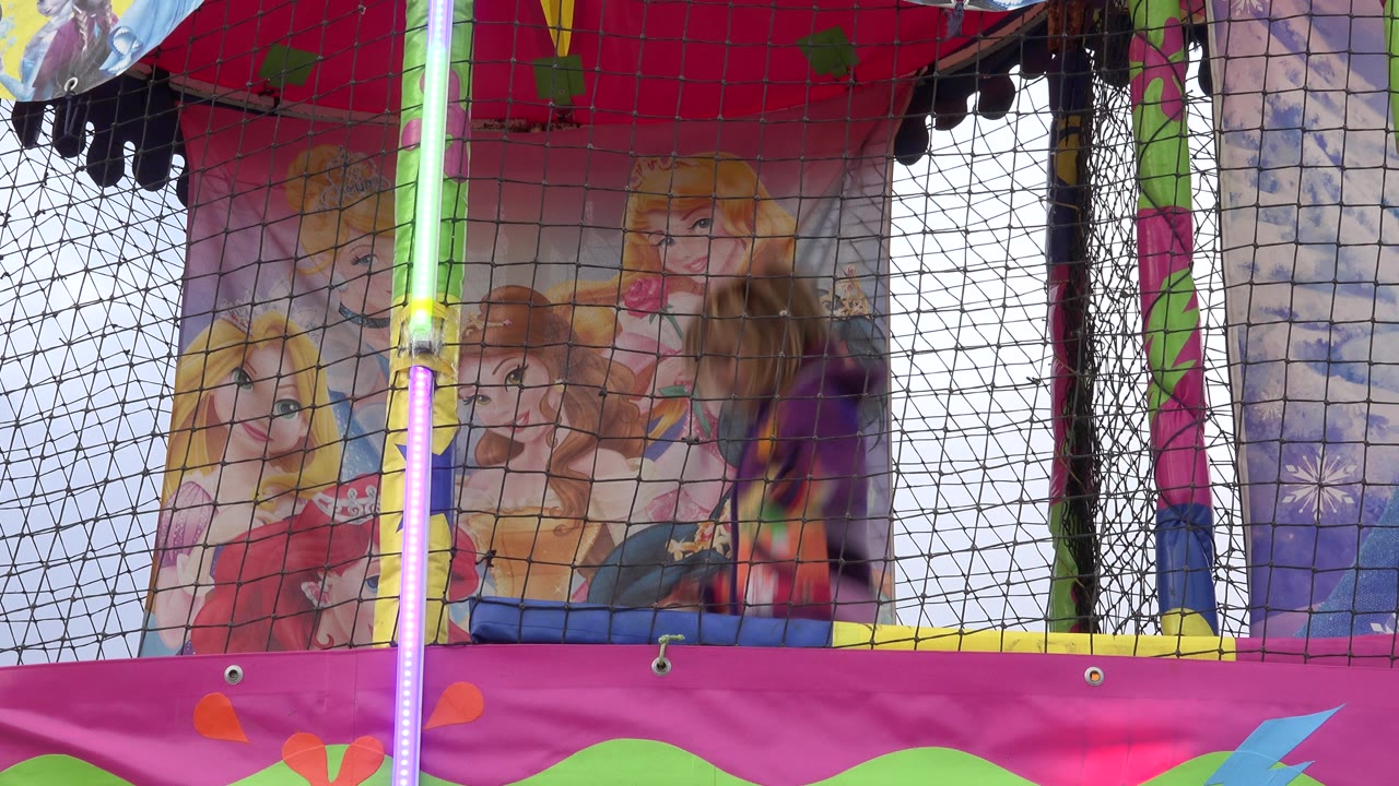 Girl bouncing inside a netted trampoline with pink padding and character artwork behind her.