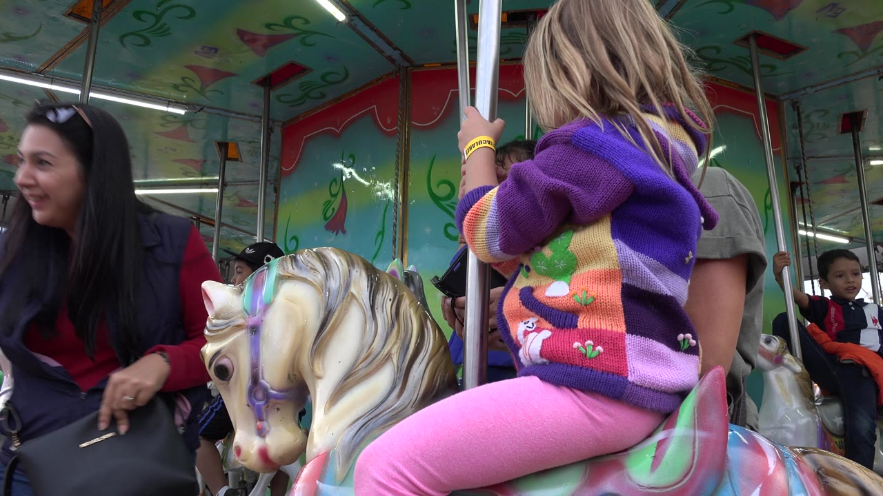 Smiling woman approaches child seated on carousel horse.
