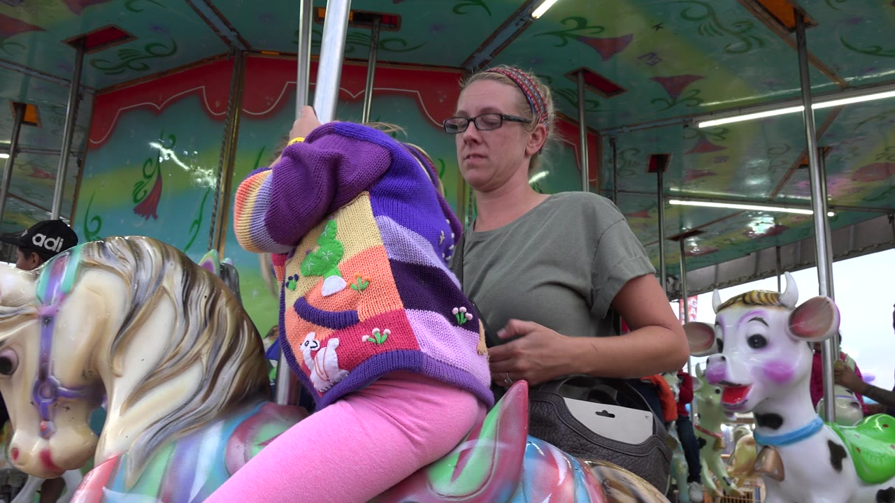 Child on a carousel horse beside an adult woman.