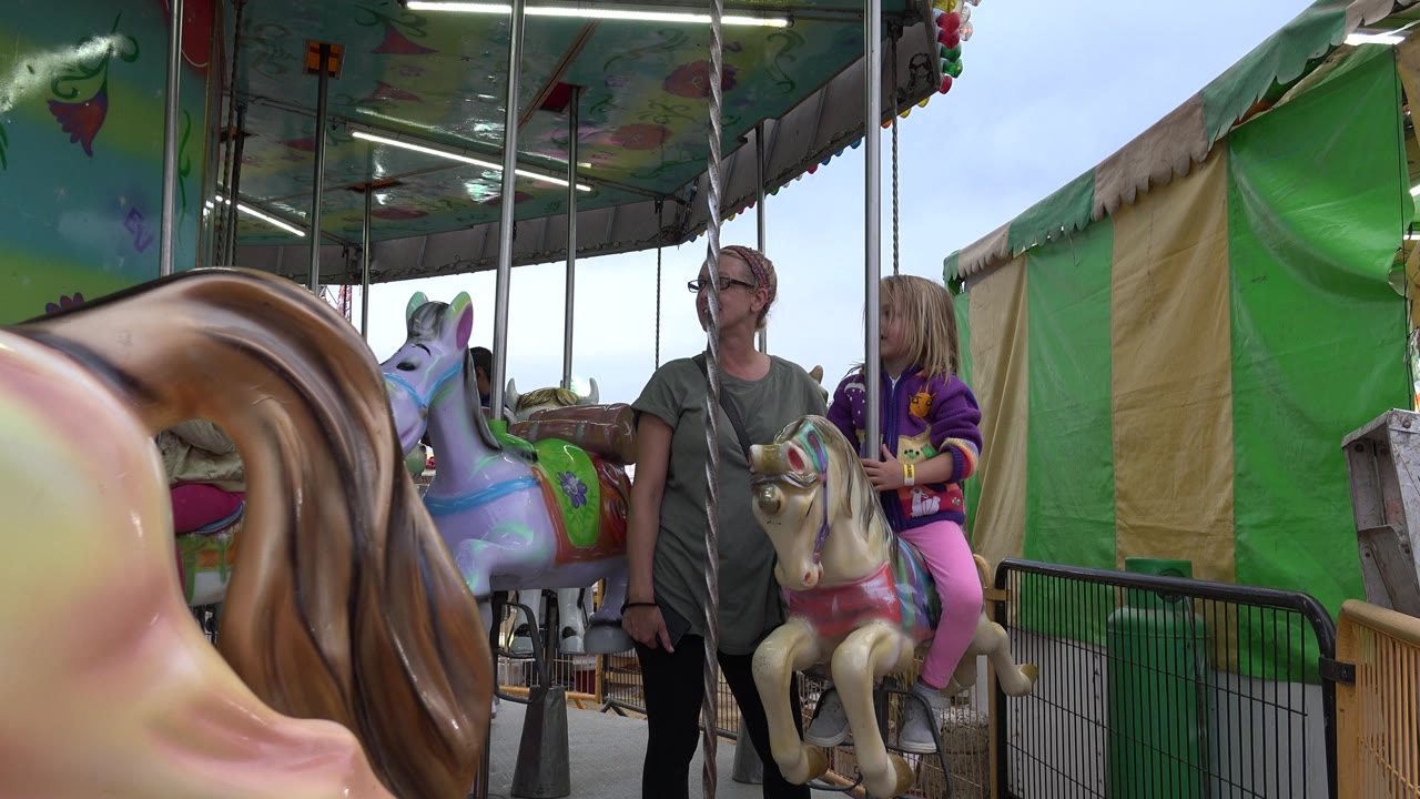 Woman standing beside a child on a carousel horse
