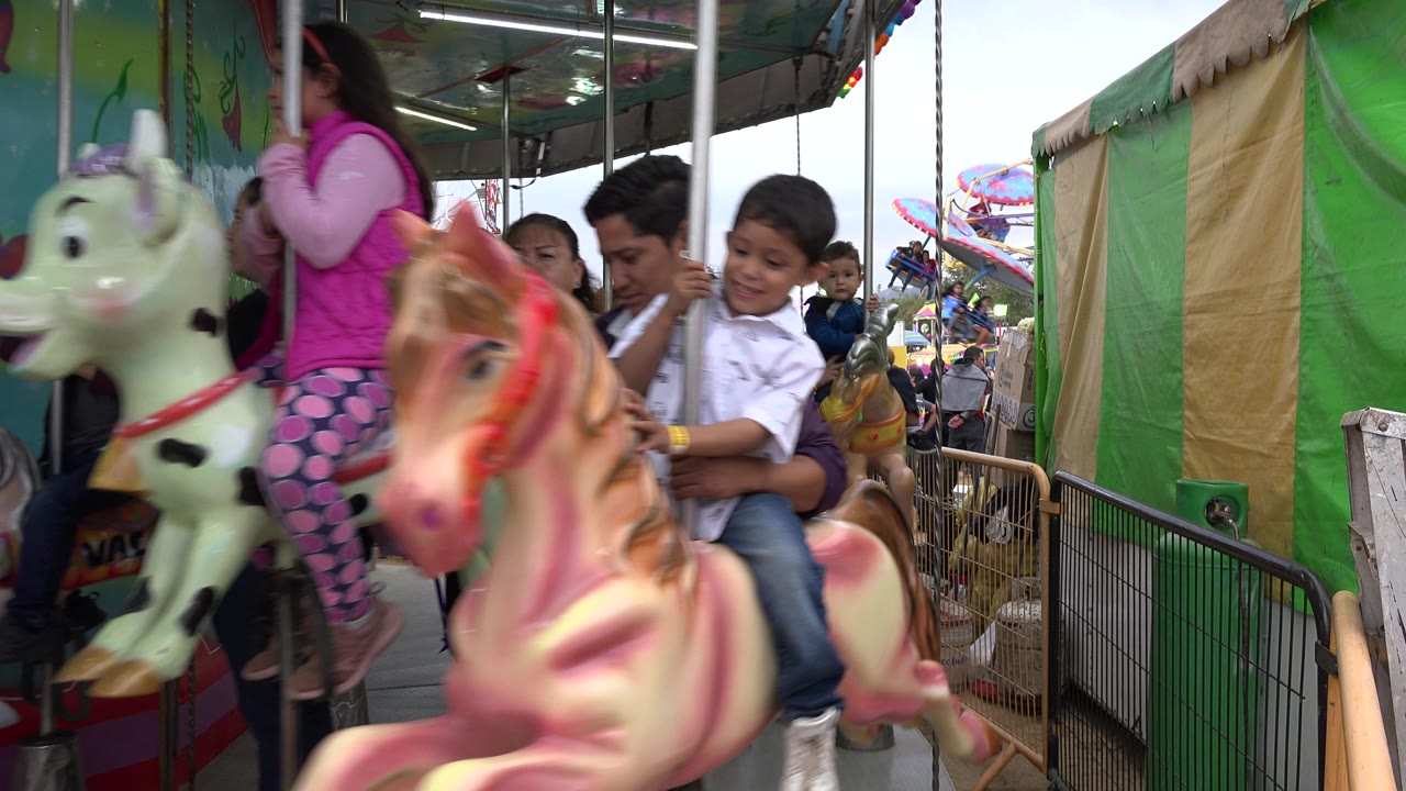 Girl and boy riding carousel animals with adults nearby.