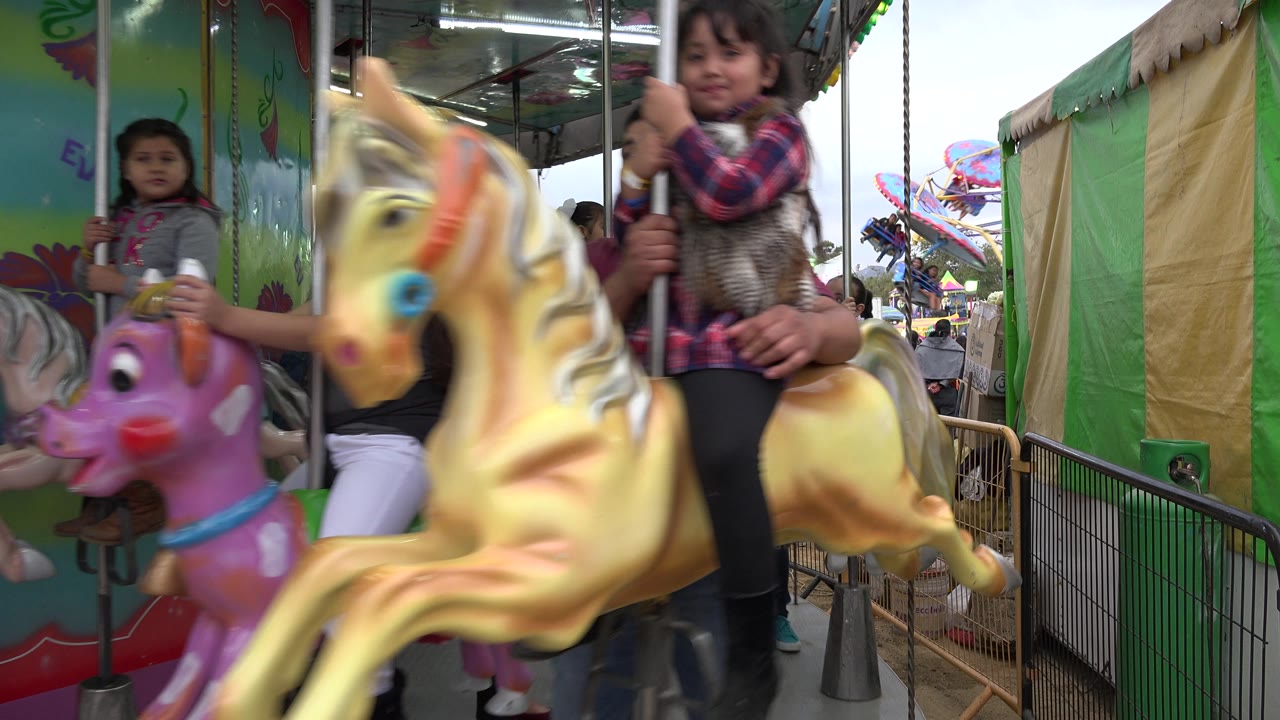 Two children ride carousel animals while an adult sits behind a gold horse.