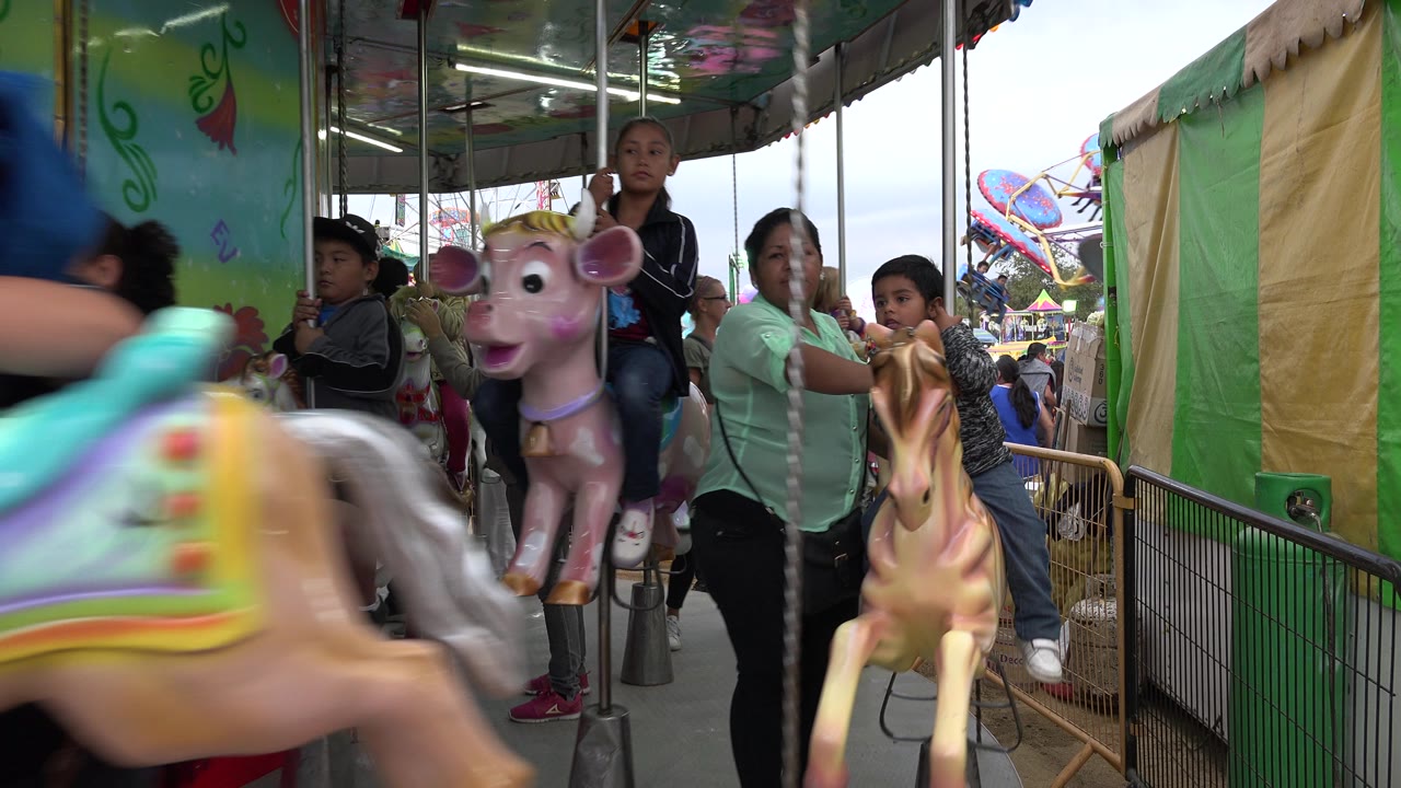 A blurred carousel horse crosses the foreground as children and parents remain visible on the ride in San Jose del Cabo, Mexico.