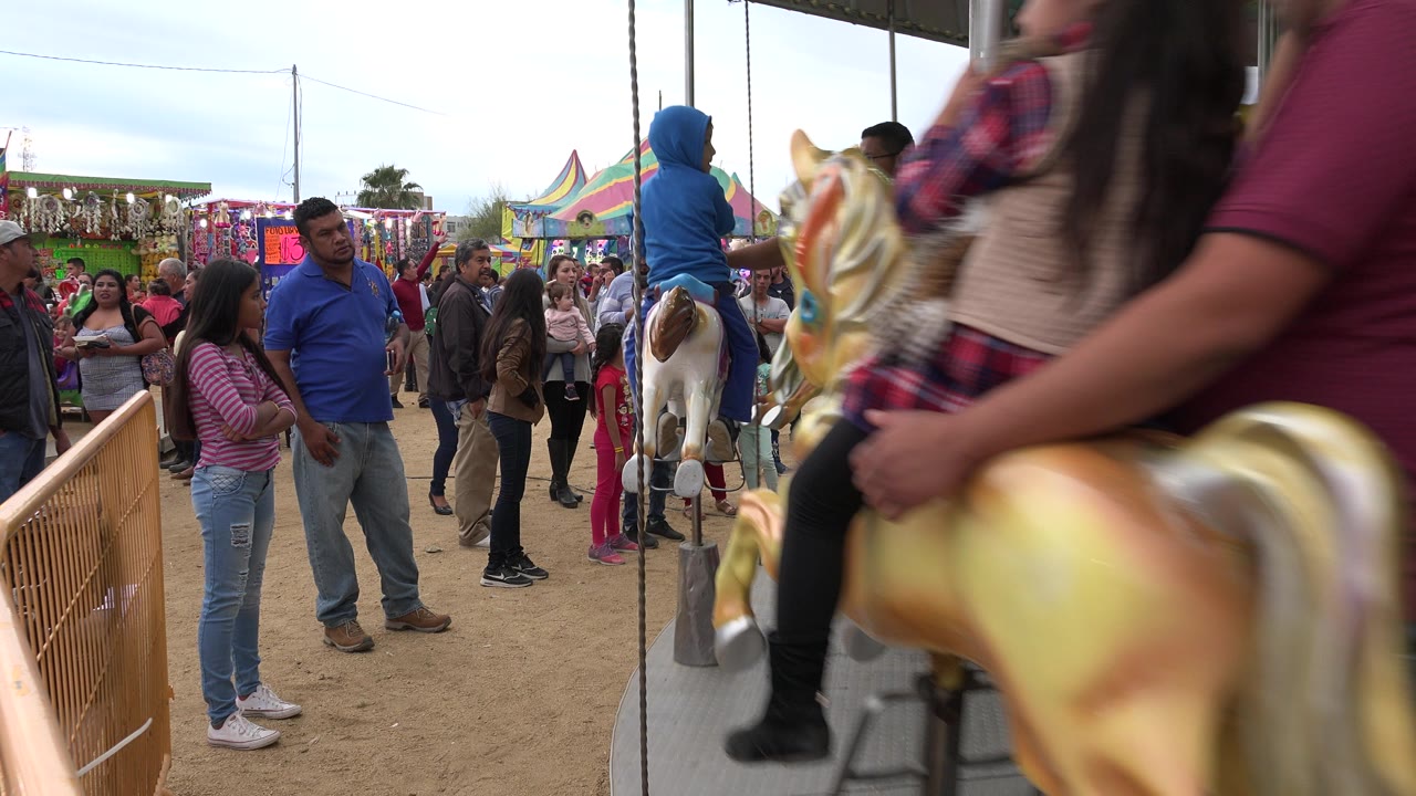Families gathered beside a merry-go-round at a fair.