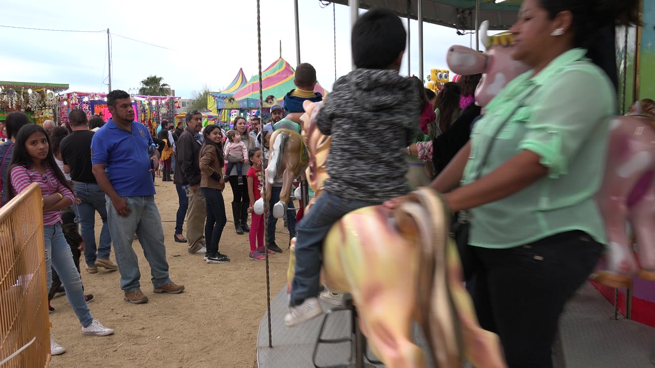 Carousel riders pass beside a crowded fair walkway.