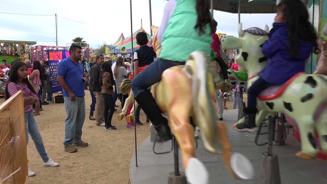 Children ride carousel horses while families wait beside the ride.