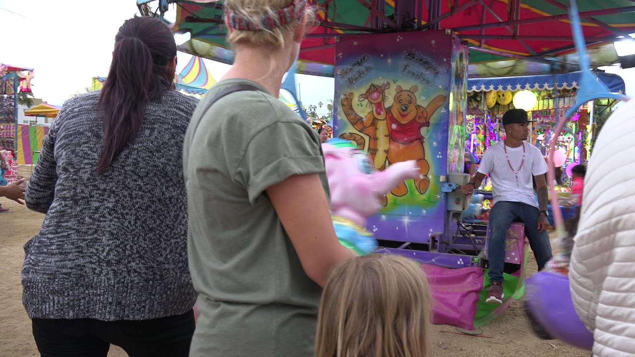 Adults and children beside a colorful merry-go-round at a fair.