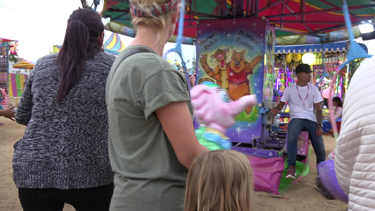 Foreground adults and a child watch a small carousel in San Jose del Cabo, Mexico, while a seated attendant is visible near the painted center column.