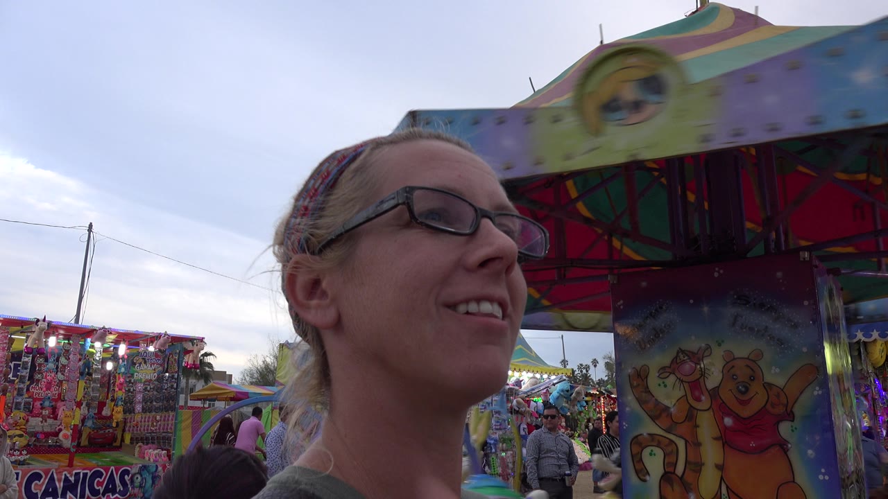 Woman in glasses beside a colorful kiddie amusement ride.