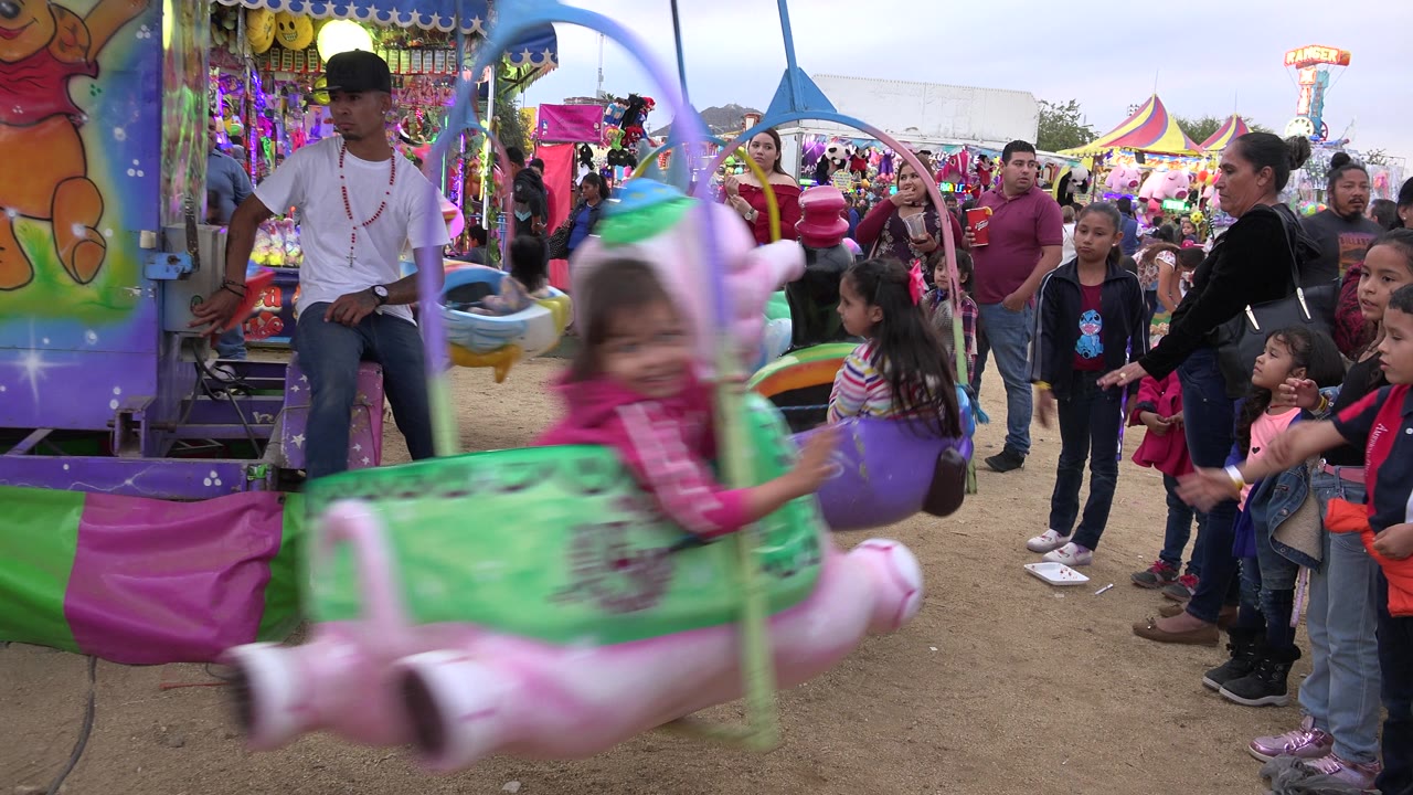 Pink and green carnival seat swings past a group of families.