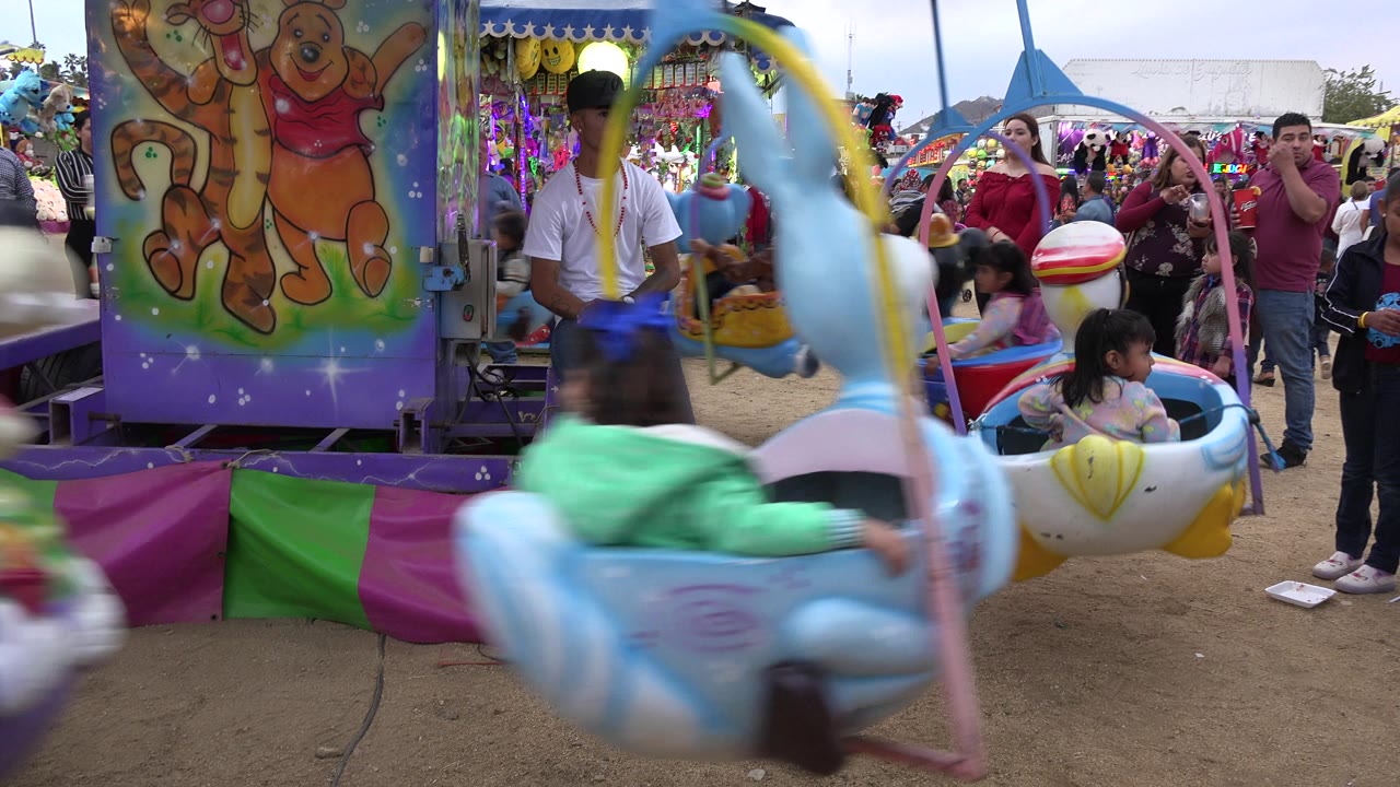 Children ride a colorful carousel beside waiting adults at a fairground.