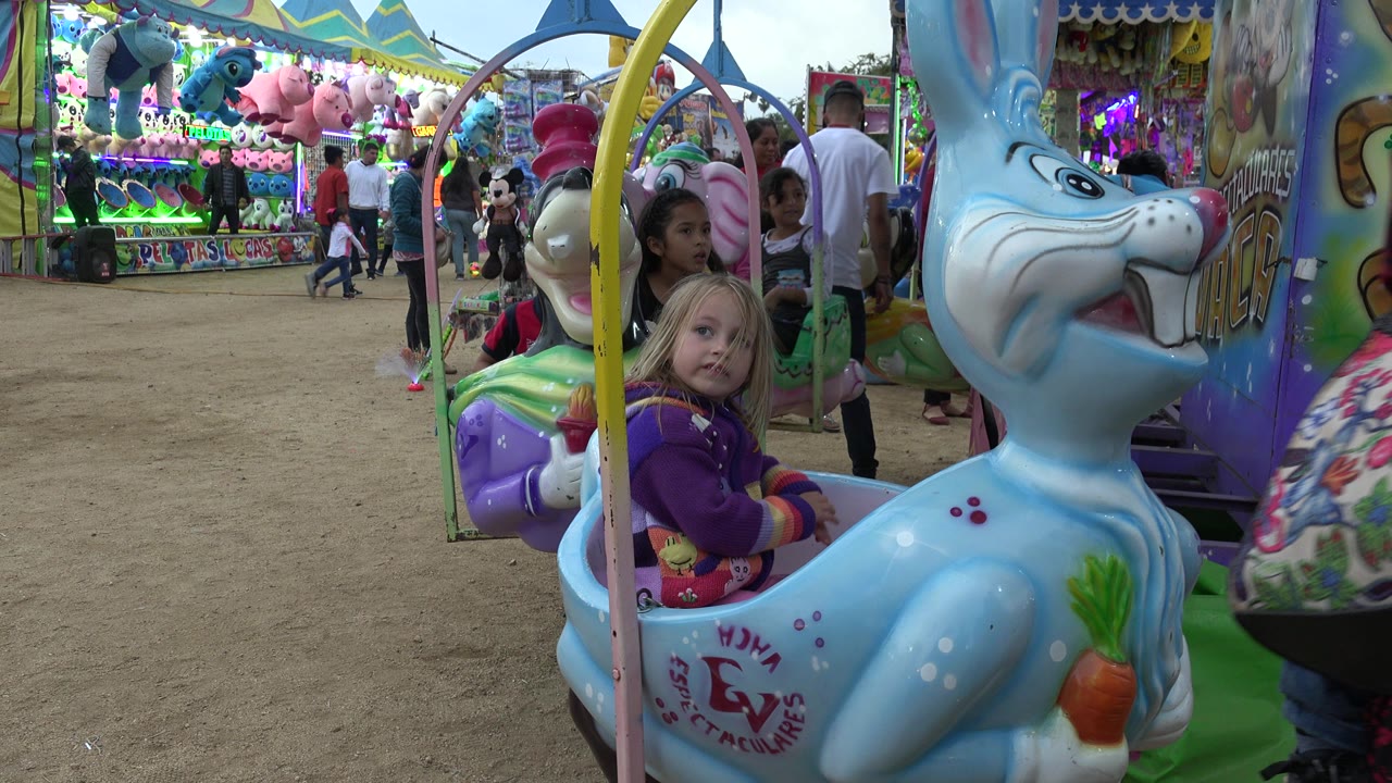 Young girl riding a blue rabbit amusement car at a colorful park ride.