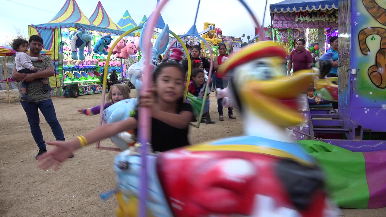 Child riding a colorful carousel animal at a carnival with adults nearby.