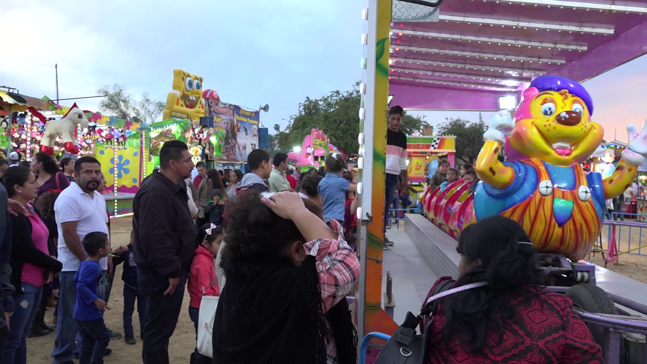 Crowd beside a colorful children's ride at a fair.