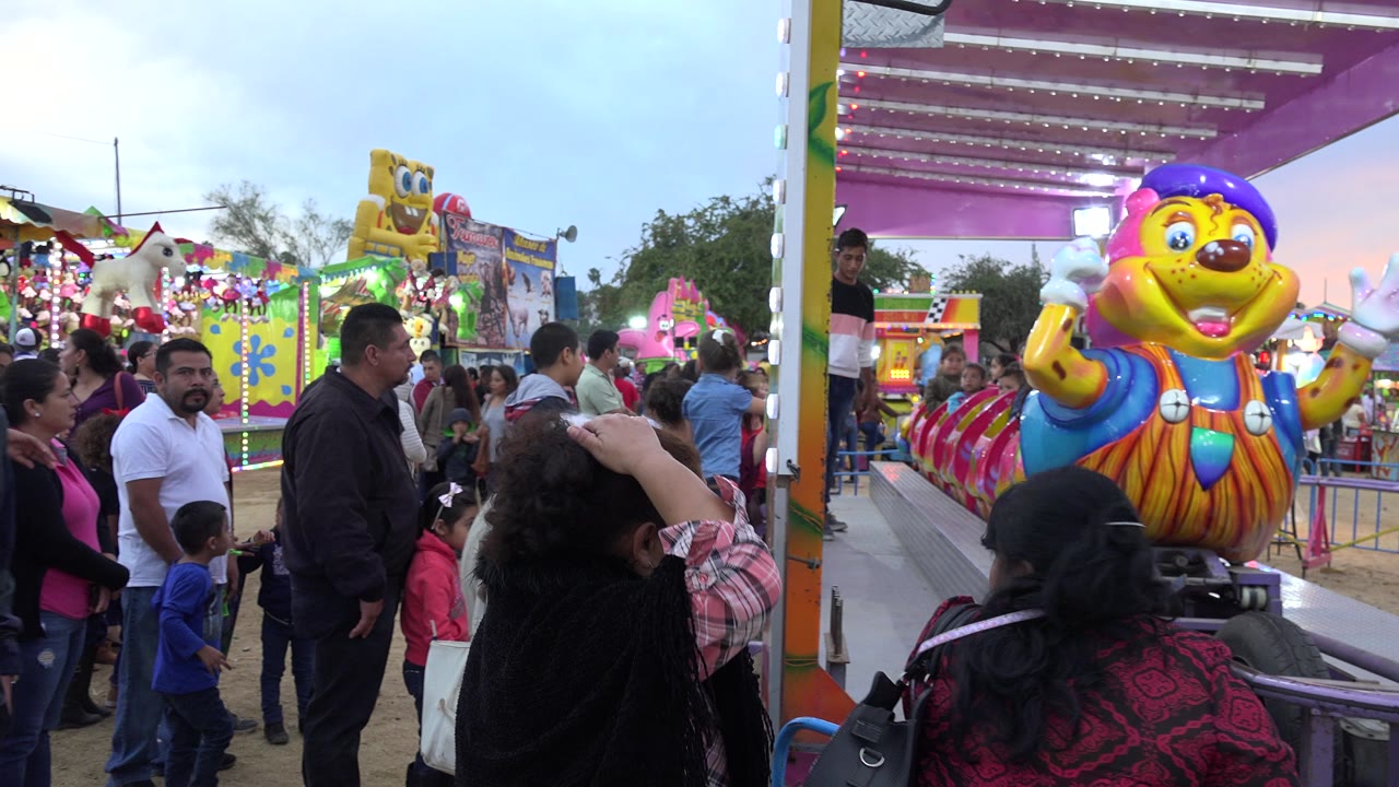 A male worker stands on the ride platform in San Jose del Cabo, Mexico, near a bright caterpillar-style children's attraction as parents and children watch.