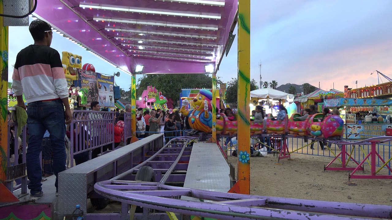 Small character roller coaster track under a purple-lit canopy at a fairground.