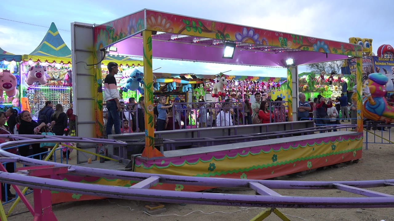 Colorful caterpillar ride beside a carnival prize booth with people watching.