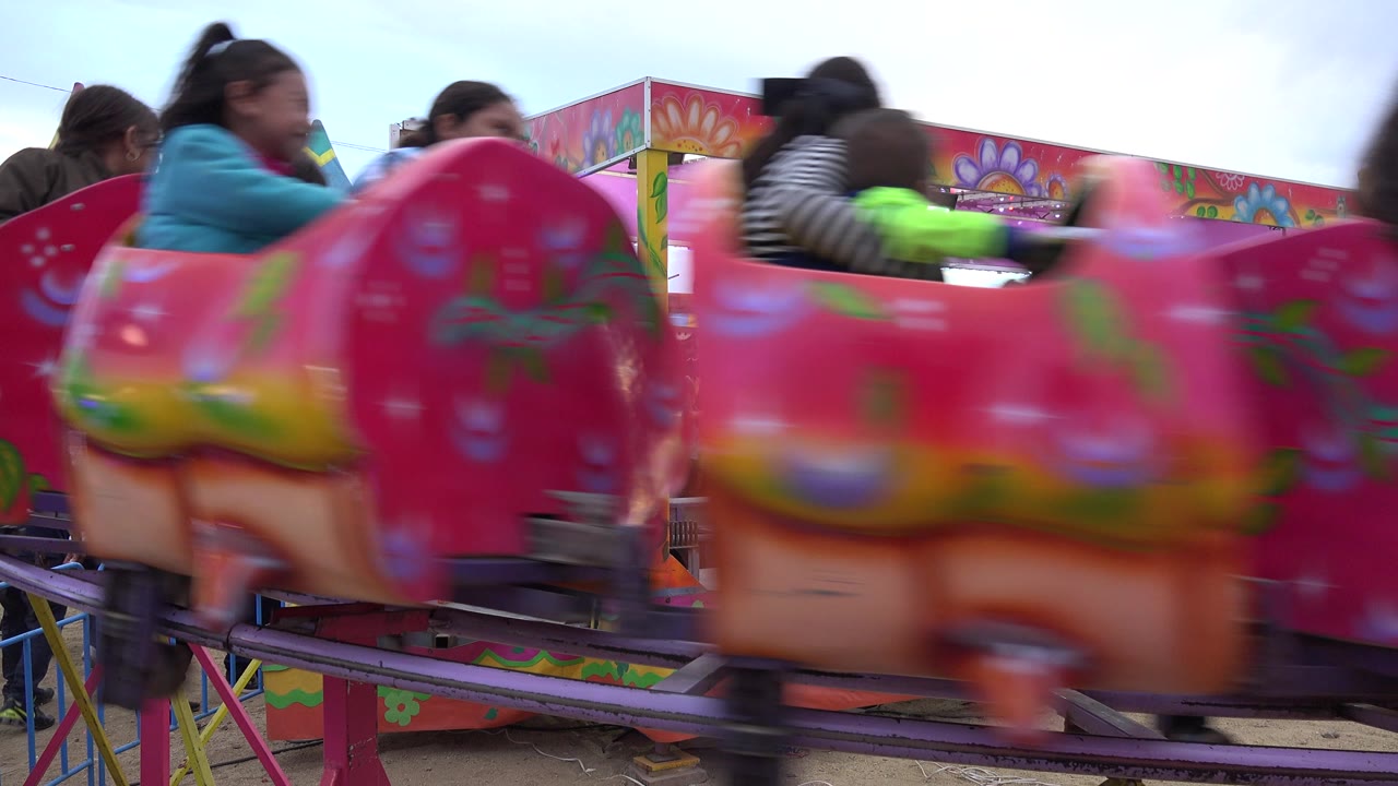 Blurred pink amusement ride cars passing in front of riders and fair booths.
