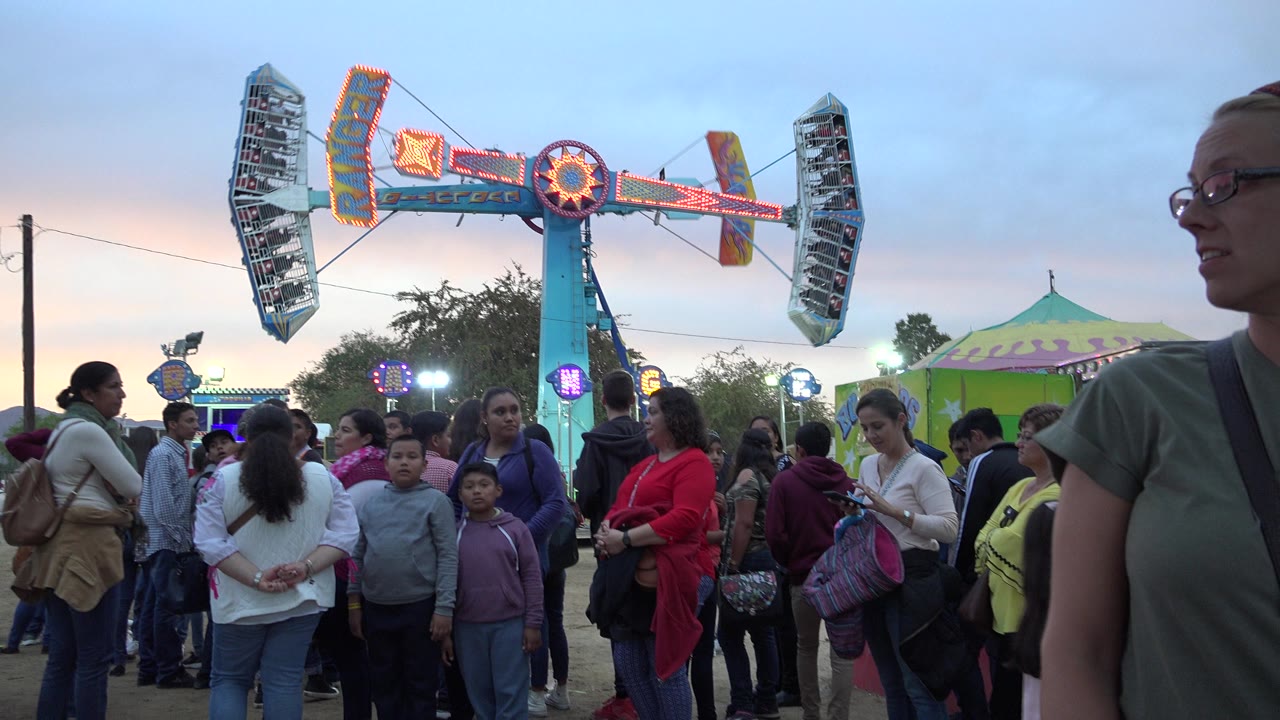 Crowd waiting below a lit carnival ride at dusk.