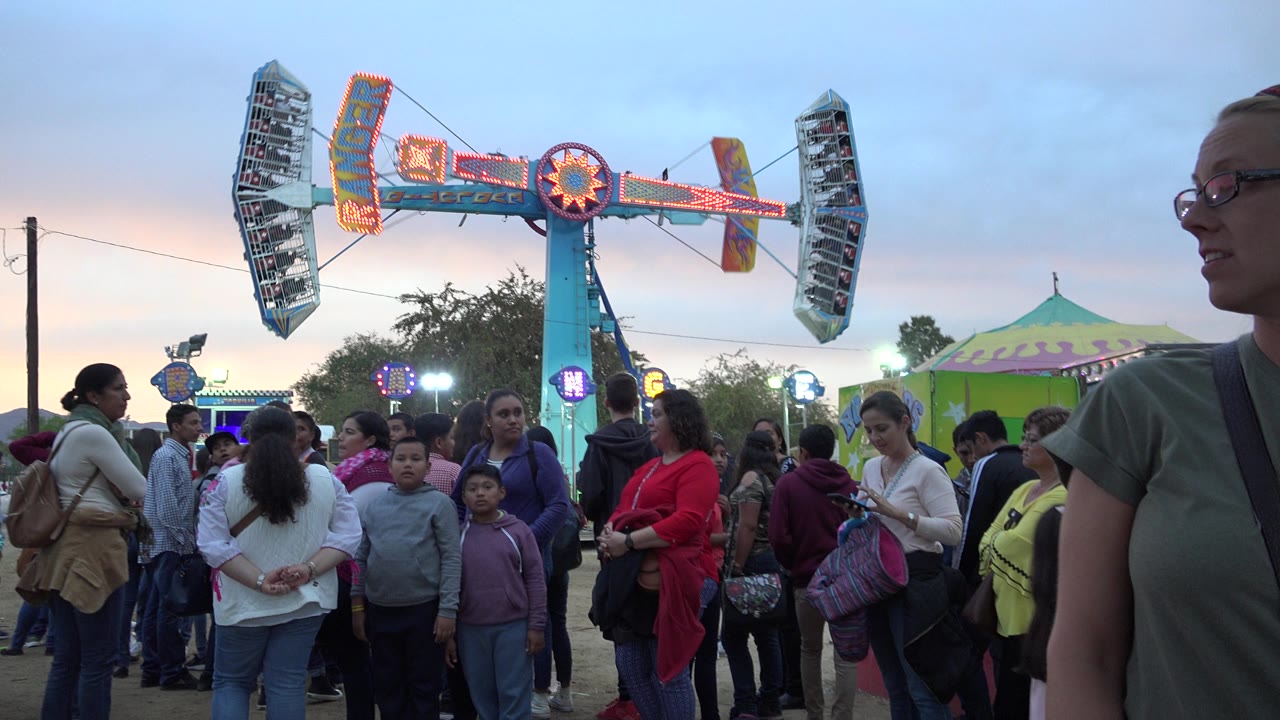 A woman passes near the right foreground while families and children stand beneath the illuminated carnival ride in San Jose del Cabo.