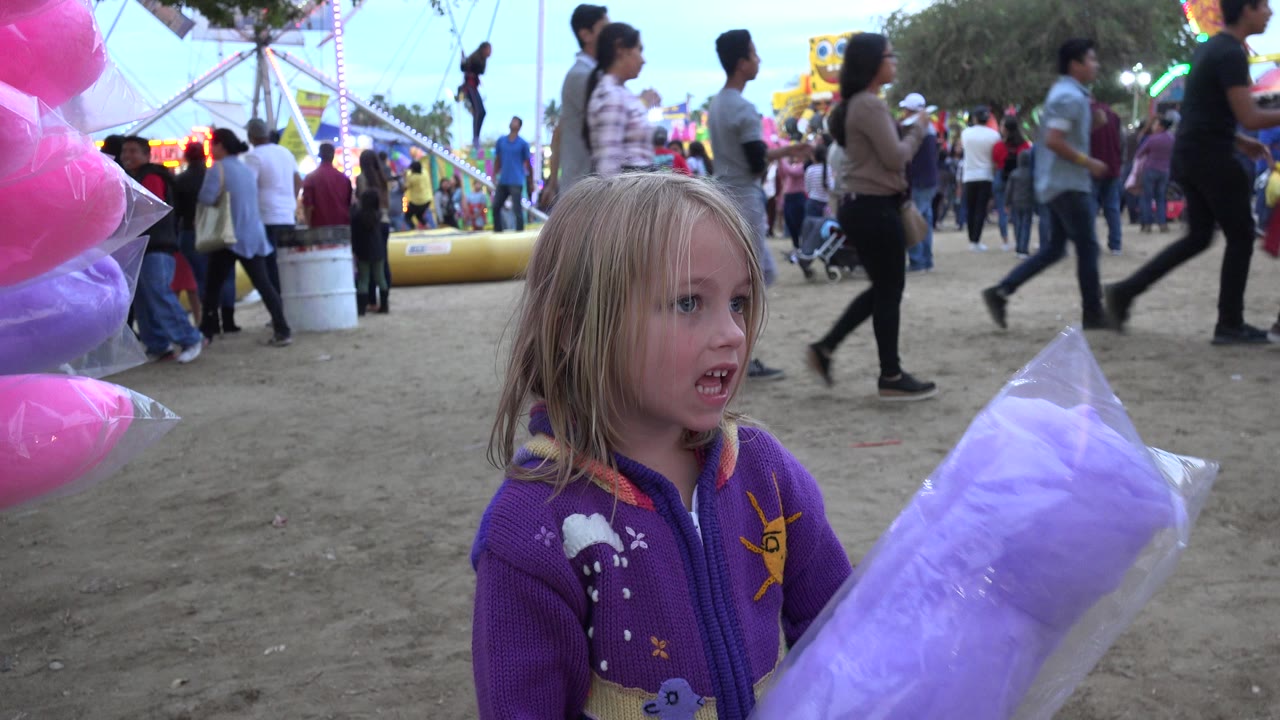 The child faces the large purple cotton candy bag while adults and children pass behind her at the San Jose del Cabo carnival.