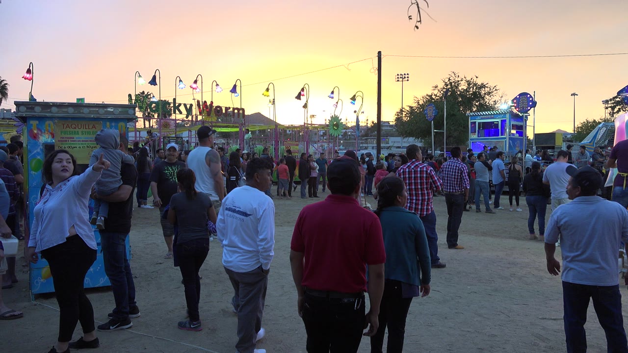 Crowd walking through a carnival midway at sunset.
