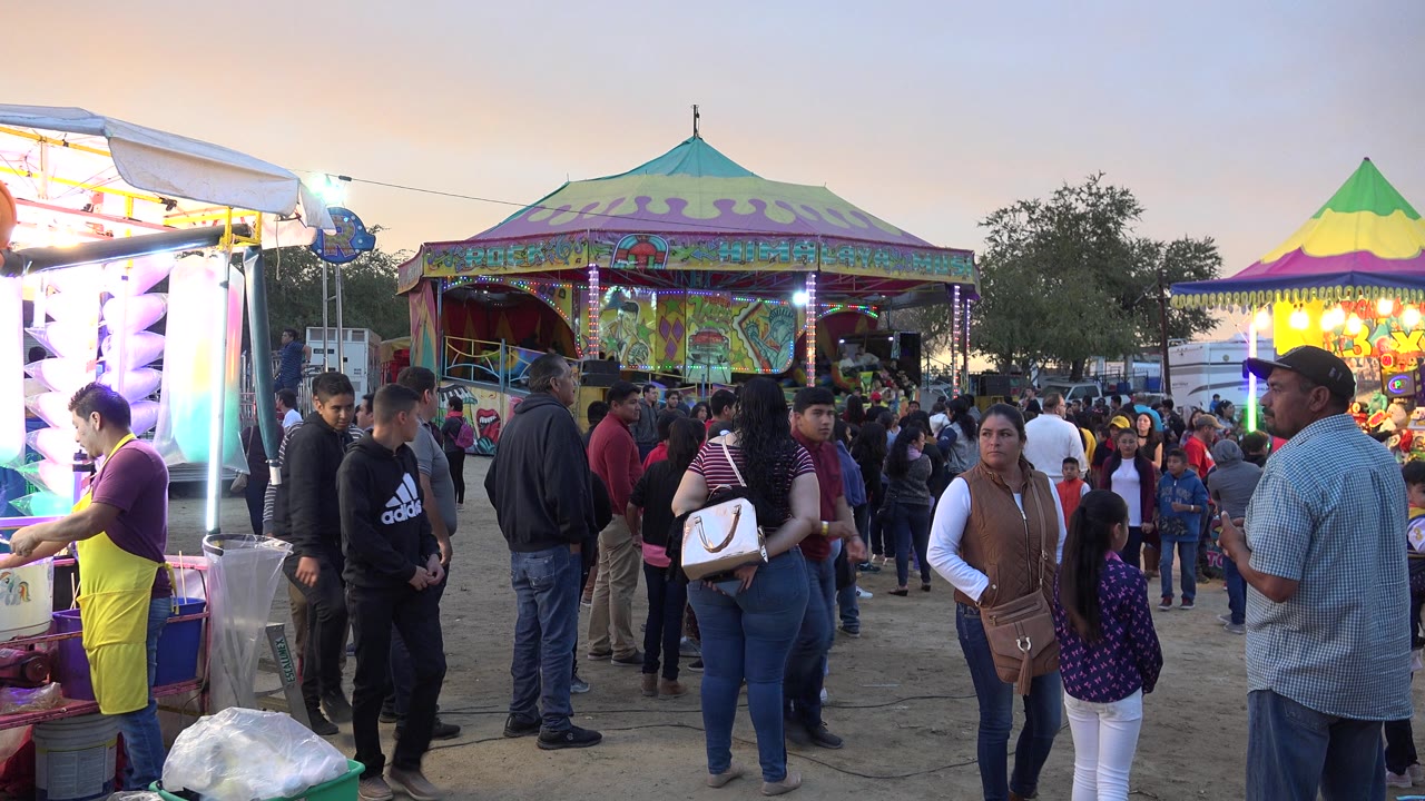 Crowd passing colorful carnival attractions at dusk